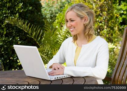 Beautiful happy smiling young woman teenage girl using a white laptop computer in her garden at home