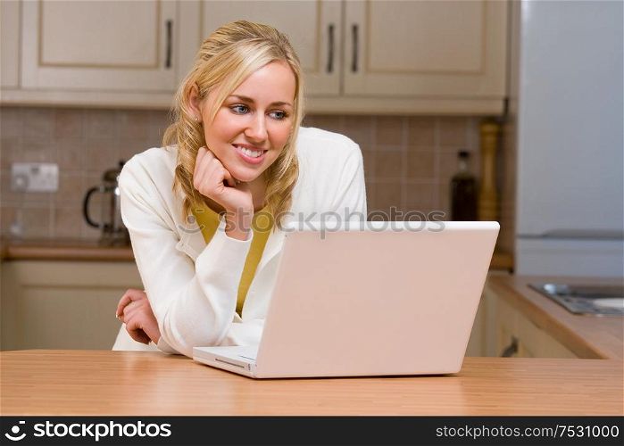 Beautiful happy smiling young woman teenage girl using a white laptop computer in her kitchen at home