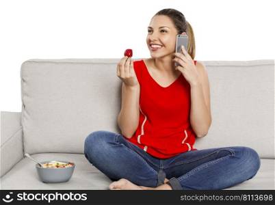 Beautiful happy woman at home making a phone call while eating strawberries