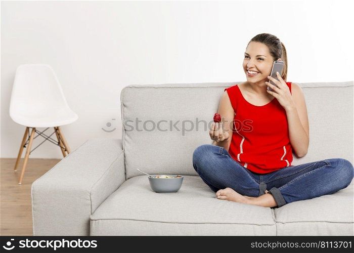 Beautiful happy woman at home making a phone call while eating strawberries