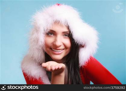 Beautiful happy woman wearing santa clause costume clothes blowing on hand sending a kiss on blue background