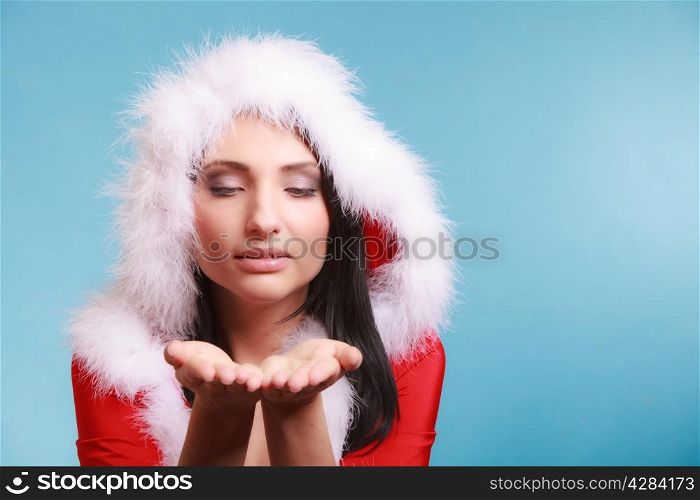 Beautiful happy woman wearing santa clause costume clothes blowing on hand sending a kiss on blue background