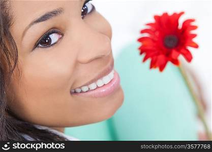 Beautiful happy young African American woman or girl smiling and holding a red gerbera daisy flower