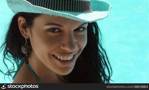 Beautiful happy young hispanic woman in straw hat smiling and relaxing near hotel pool.