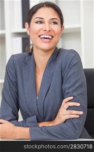 Beautiful happy young Latina Hispanic woman or businesswoman in smart business suit sitting at a desk in an office laughing