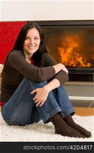 Beautiful happy young woman sitting front of home fireplace