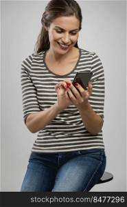 Beautiful happy young woman sitting on a bench and sendind a text message to someone