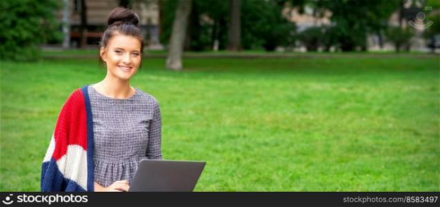 Beautiful happy young woman sitting on the bench with a laptop in the park. Woman sitting with a laptop