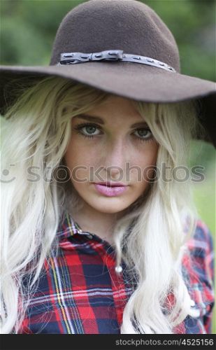 Beautiful healthy young woman outdoors wearing big floppy hat and checked shirt