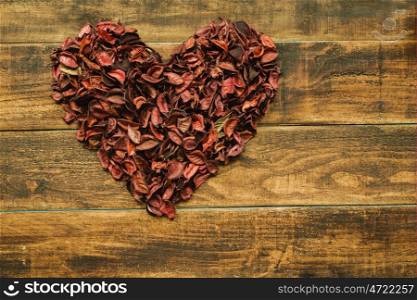 Beautiful heart maked with dry petals on a wooden rustic table