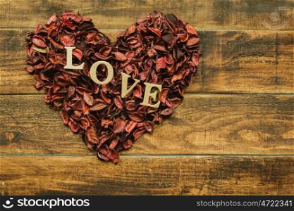 Beautiful heart maked with dry petals on a wooden rustic table