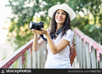 Beautiful hiker young woman taking photographs with a mirrorless camera, wearing straw hat, hiking in the countryside.. Hiker woman taking photographs with a mirrorless camera