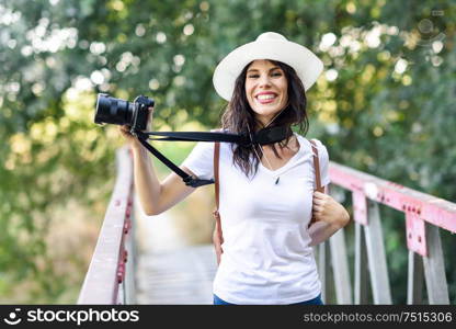 Beautiful hiker young woman taking photographs with a mirrorless camera, wearing straw hat, hiking in the countryside.. Hiker woman taking photographs with a mirrorless camera