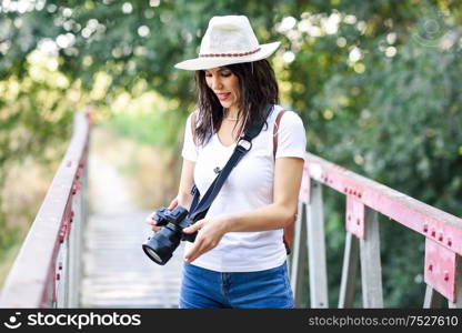 Beautiful hiker young woman taking photographs with a mirrorless camera, wearing straw hat, hiking in the countryside.. Hiker woman taking photographs with a mirrorless camera