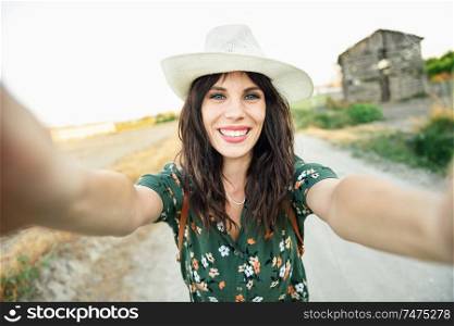 Beautiful hiker young woman, wearing flowered shirt, taking a selfie photograph outdoors. Hiker young woman taking a selfie photograph outdoors