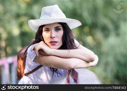 Beautiful hiker young woman with backpack, with blue eyes, wearing straw hat, hiking in the countryside and having fun on a rural bridge.. Woman with backpack standing on rural bridge.