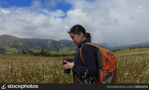 Beautiful Hispanic female explorer seen from behind with backpack reviewing photos on her camera in the middle of a sown field on a cloudy morning. Beautiful Hispanic female explorer seen from behind with backpack reviewing photos on her camera in the middle of a sown field