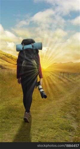 Beautiful Hispanic female explorer seen from behind with backpack walking with a camera in hand in the middle of a sown field on a cloudy morning. Beautiful Hispanic female explorer seen from behind with backpack walking with a camera in hand in the middle of a sown field