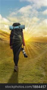 Beautiful Hispanic female explorer seen from behind with backpack walking with a camera in hand in the middle of a sown field on a cloudy morning. Beautiful Hispanic female explorer seen from behind with backpack walking with a camera in hand in the middle of a sown field