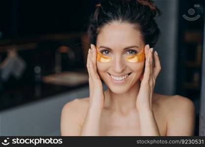 Beautiful hispanic girl doing spa procedures and touches her temples skin. Portrait of happy young lady which applies collagen eye patches. Golden anti age and anti wrinkle patches.. Beautiful hispanic girl doing spa procedures. Lady applies patches, touches temples and eyes skin.