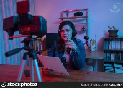 Beautiful Hispanic woman in front of a video camera recording a blog in her studio with red and blue lights inside her house. Streaming a speech on social media. Beautiful Hispanic woman in front of a video camera recording a blog in her studio with red and blue lights inside her house