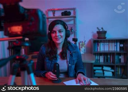 Beautiful Hispanic woman in front of a video camera recording a blog in her studio with red and blue lights inside her house. Streaming a speech on social media. Beautiful Hispanic woman in front of a video camera recording a blog in her studio with red and blue lights inside her house