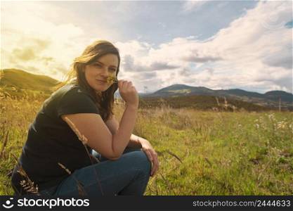 Beautiful Hispanic woman sitting looking at the camera in the middle of the field smelling yellow flowers that she is holding in her hand during sunset. Beautiful Hispanic woman sitting in the middle of the field smelling yellow flowers that she is holding in her hand during sunset