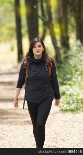 Beautiful Hispanic woman with backpack walking alone on a forest path during the morning. Beautiful Hispanic woman with backpack walking alone on a forest path