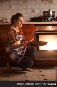 Beautiful housewife sitting next to oven and holding pan near hot oven