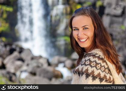 Beautiful Icelandic woman wearing traditionally patterned knitwear smiling in the mountains by a waterfall in Northern Iceland