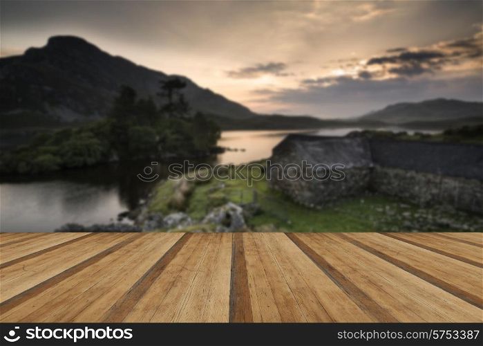 Beautiful image of stone barn with mountains and lake at sunrise. Beautiful sunrise reflected in calm Lakes landscape with wooden planks floor