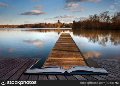 Beautiful image of sunset landscape of wooden fishing jetty on calm lake with clear reflections coming out of pages in magic book