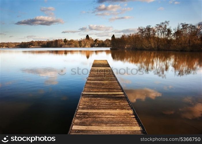Beautiful image of sunset landscape of wooden fishing jetty on calm lake with clear reflections