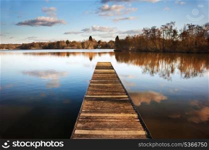 Beautiful image of sunset landscape of wooden fishing jetty on calm lake with clear reflections