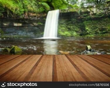 Beautiful image of waterfall in forest with stram and lush green foliage with wooden planks floor