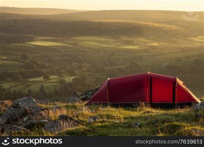 Beautiful image of wild camping in English countryside during stunning Summer sunrise with warm glow of the sun lighting the landscape