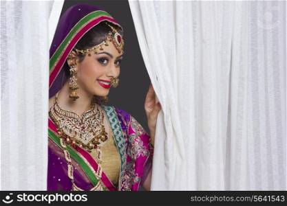 Beautiful Indian bride smiling amidst curtains