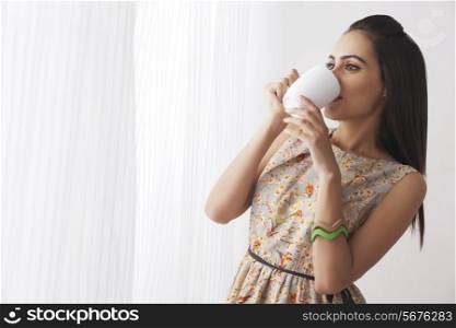 Beautiful Indian woman drinking coffee by curtains