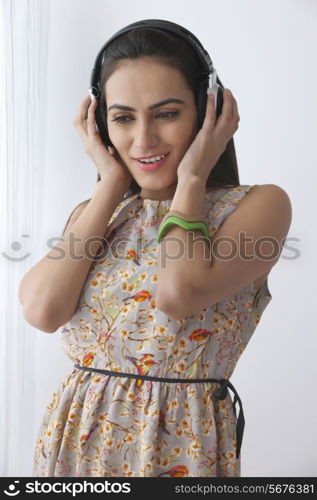Beautiful Indian woman listening to headphones by curtain