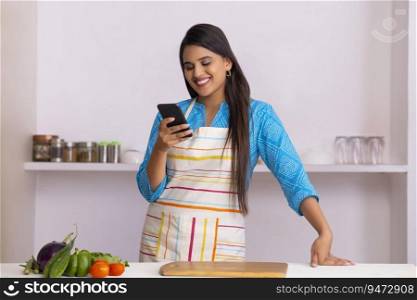Beautiful Indian woman watching smartphone in the kitchen
