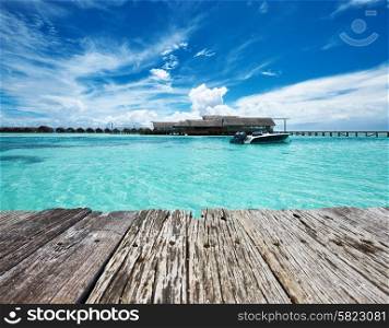 Beautiful island beach and old wooden pier with motor boat at Maldives