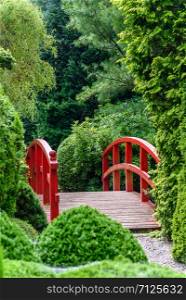 Beautiful Japanese garden with red wooden bridge among green trees