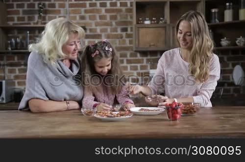 Beautiful joyful mother having fun with her smiling little daughter staining her nose with chocolate while family preparing cookies in the kitchen. Multi generation family cooking sweets together during weekend. Dolly shot. Slow motion.
