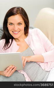 Beautiful joyful woman holding digital tablet lying on couch