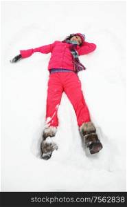 Beautiful joyful young woman in pink clothes laying down on a snow on vacation during a sunny winter day. Young woman laying down on snow