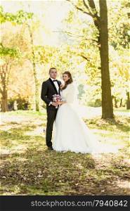 Beautiful just married couple embracing at park at autumn sunny day