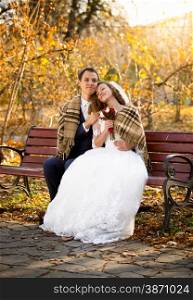 Beautiful just married couple sitting on bench at autumn park