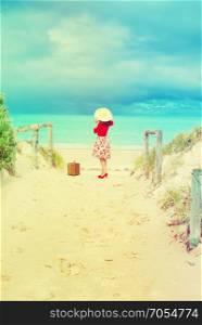 Beautiful lady in red traveler with wicker suitcase on the beach in retro style