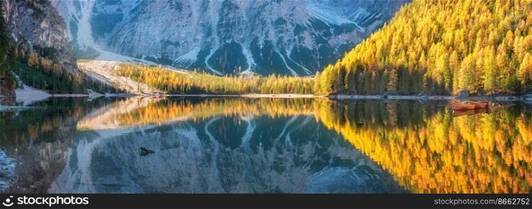 Beautiful lake with perfect reflection in water in autumn. Braies lake at sunrise in fall. Dolomites, Italy. Landscape with orange forest, mountains, lake, boats. Trees with colorful foliage. Panorama