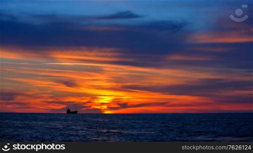 Beautiful landscape, dramatic orange sunset over sea, ship silhouette over evening sky background, beauty of summer nature